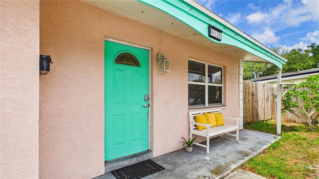 A pink house exterior features a bright teal front door and a white wooden bench — 6132 100TH CIRCLE, PINELLAS PARK, FL