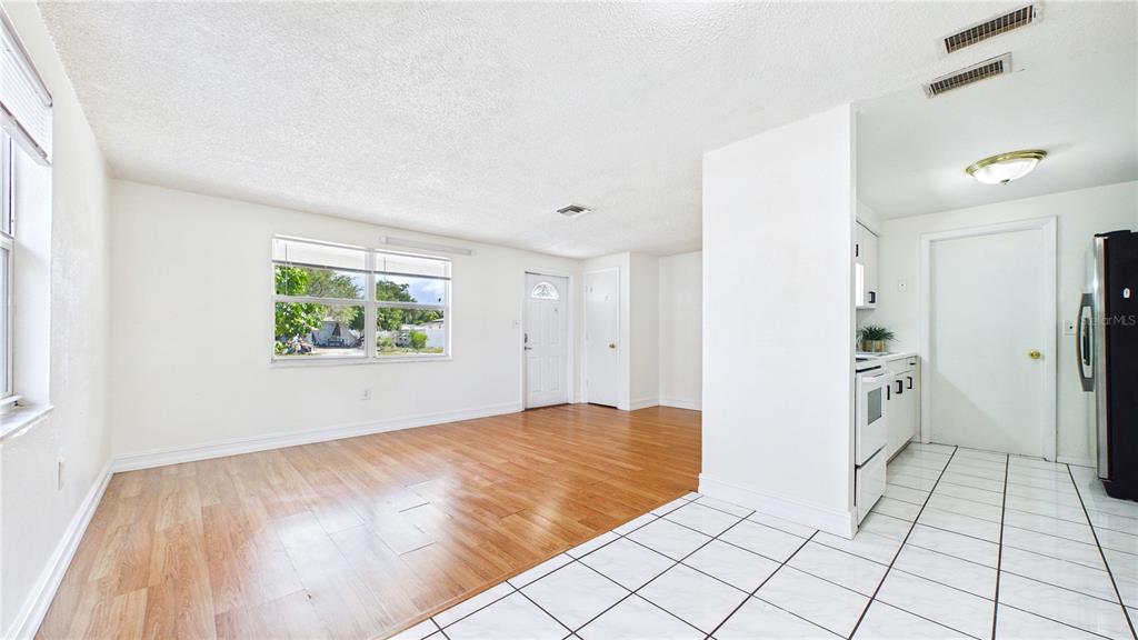 An open-concept living area features wood-look flooring, white walls, and an adjacent tiled kitchen — 6132 100TH CIRCLE, PINELLAS PARK, FL