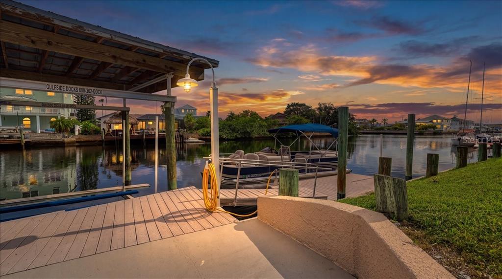 A boat dock with a covered slip and a pontoon boat at sunset — 4295 NEWPORT DRIVE, HERNANDO BEACH, FL