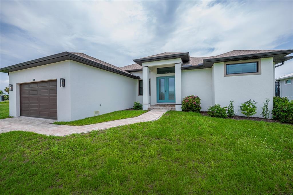 A single-story house with white stucco walls, a brown garage door, and teal double doors — 224 W PINE VALLEY LANE, ROTONDA WEST, FL