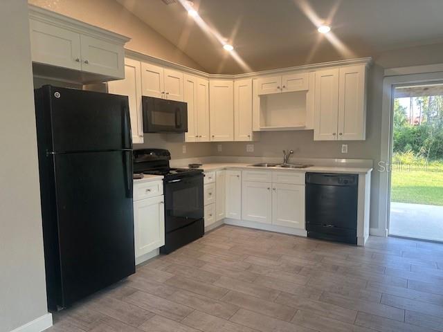 A kitchen features white cabinets, black appliances, and light wood-look tile flooring — 651 CHAMBER STREET NW, PORT CHARLOTTE, FL