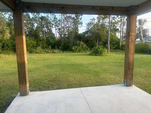 A view of a grassy backyard from a covered concrete patio with wooden support posts — 651 CHAMBER STREET NW, PORT CHARLOTTE, FL