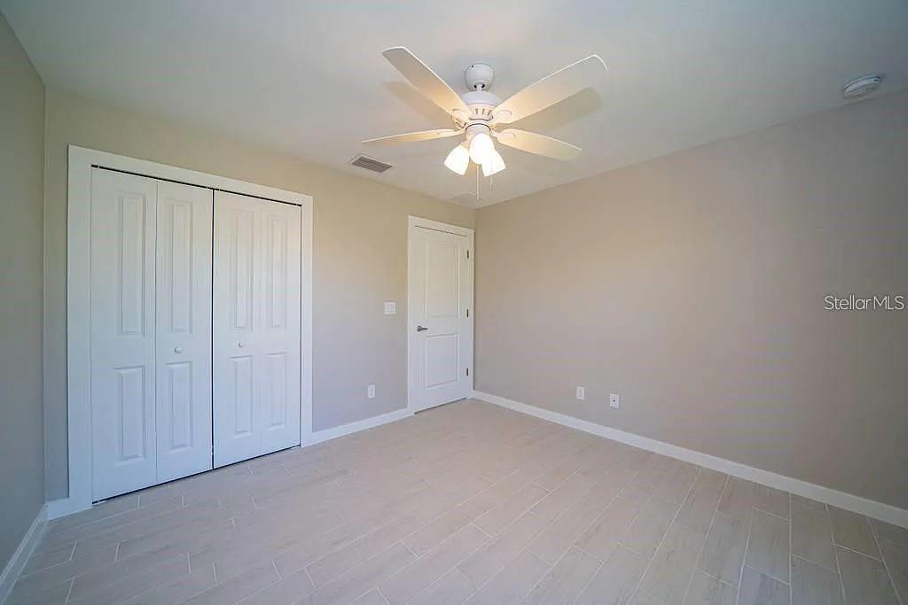 An empty bedroom features light-colored tile flooring, beige walls, a ceiling fan, and white doors — 651 CHAMBER STREET NW, PORT CHARLOTTE, FL