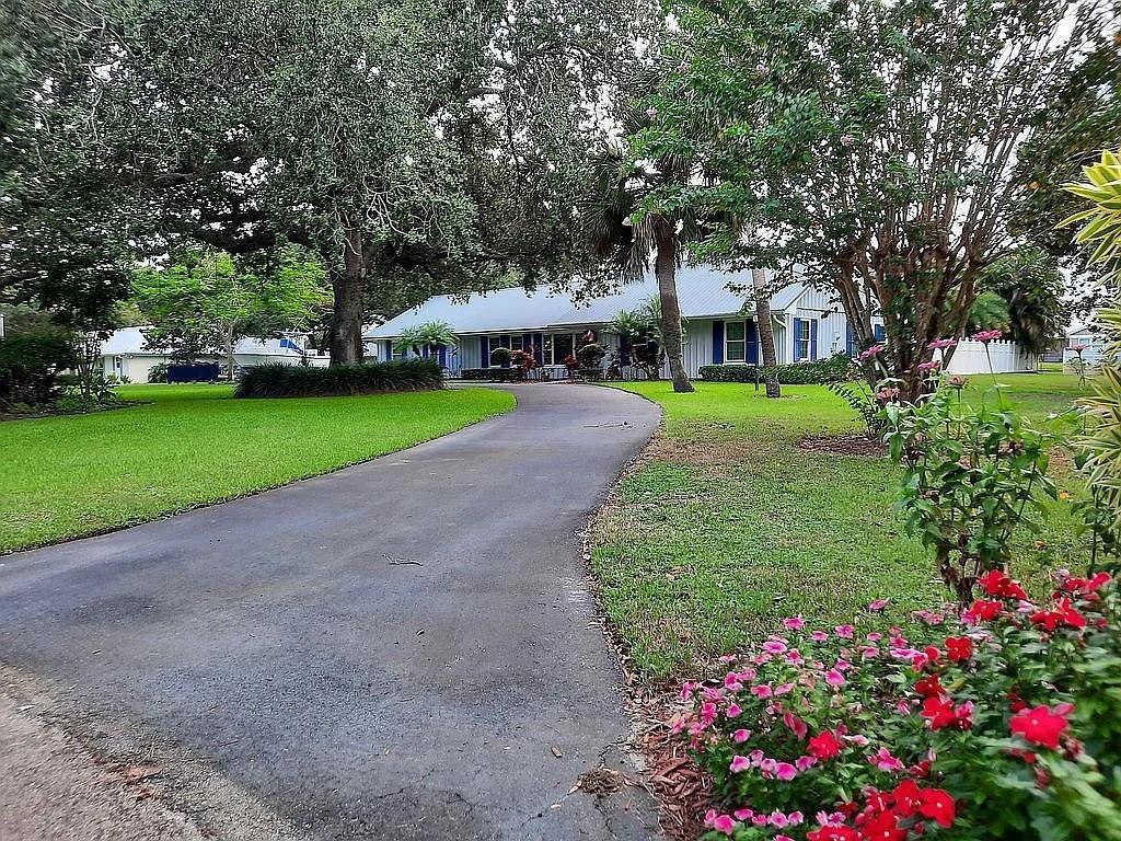 A curved driveway leads to a single-story house surrounded by large trees and green lawns — 155 31st Avenue, Vero Beach FL 32968, VERO BEACH, FL