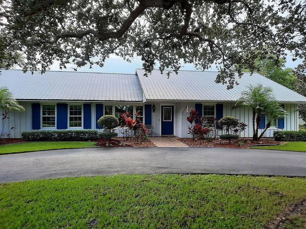A single-story house with a metal roof, blue shutters, and a curved asphalt driveway — 155 31st Avenue, Vero Beach FL 32968, VERO BEACH, FL