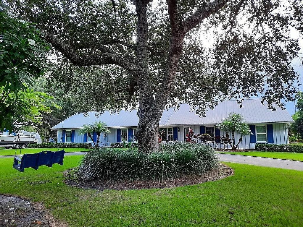 A large oak tree stands in the front yard of a single-story house with blue shutters — 155 31st Avenue, Vero Beach FL 32968, VERO BEACH, FL