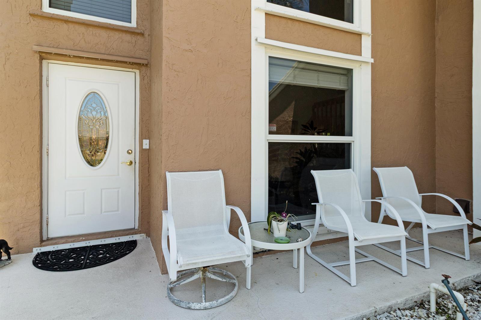 A white front door and three patio chairs sit on a concrete porch — 5525 NW 54th Circle, Coconut Creek FL 33073, COCONUT CREEK, FL
