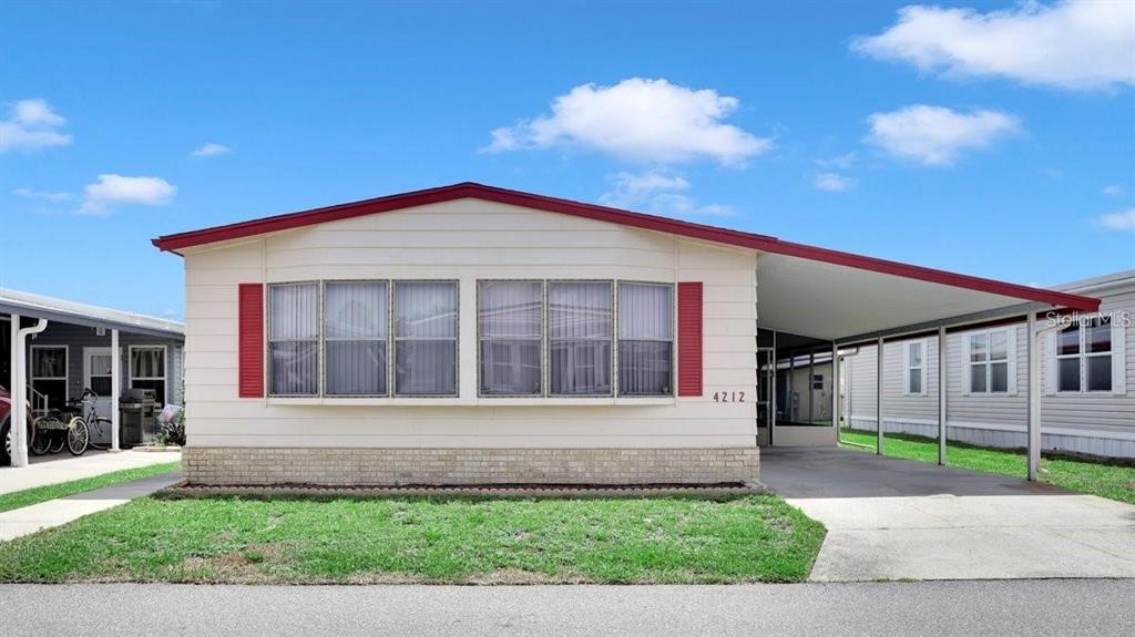 A single-story manufactured home with a red roof, beige siding, and an attached carport — 4212 CEDARWOOD STREET, WINTER HAVEN, FL