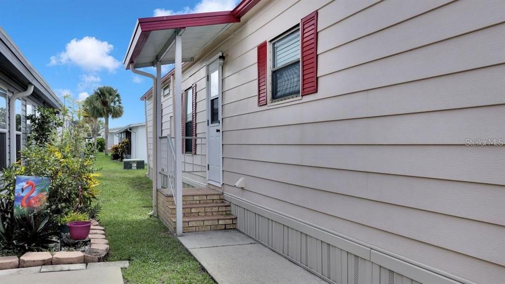 A side view of a mobile home with beige horizontal siding, red shutters, and brick steps — 4212 CEDARWOOD STREET, WINTER HAVEN, FL