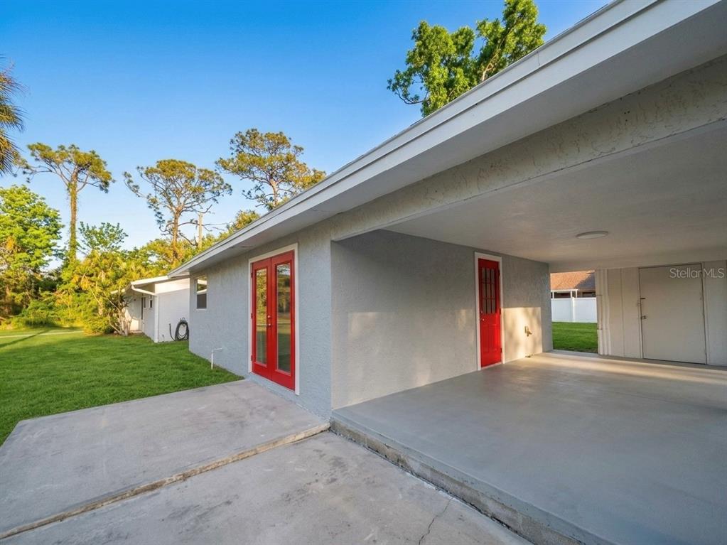 A gray house exterior features a covered carport, red double doors, and a red door — 735 BERTREND STREET, ENGLEWOOD, FL