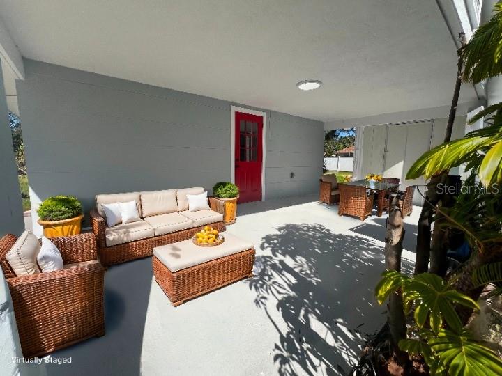 A covered patio features wicker furniture, a red door, and potted plants on a concrete floor — 735 BERTREND STREET, ENGLEWOOD, FL