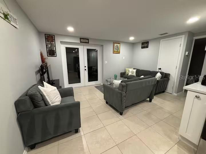 A living room with gray tile floors, a dark gray sofa, and white French doors — 735 BERTREND STREET, ENGLEWOOD, FL