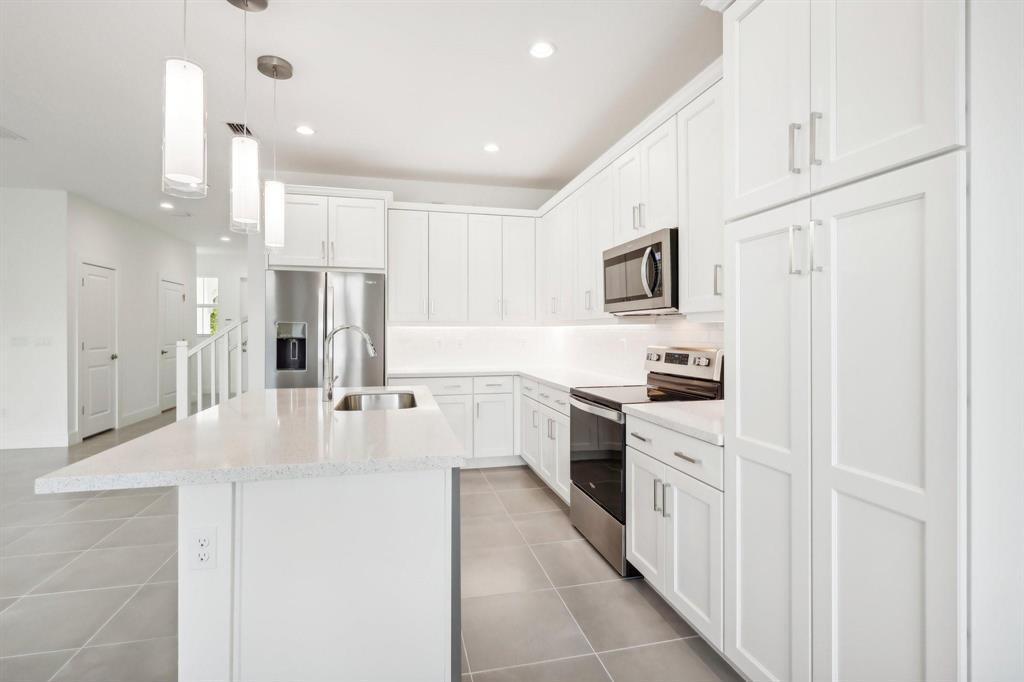 A modern kitchen features white cabinets, stainless steel appliances, a quartz island, and tile flooring — 615 Parsons Way, Deerfield Beach FL 33442, DEERFIELD BEACH, FL
