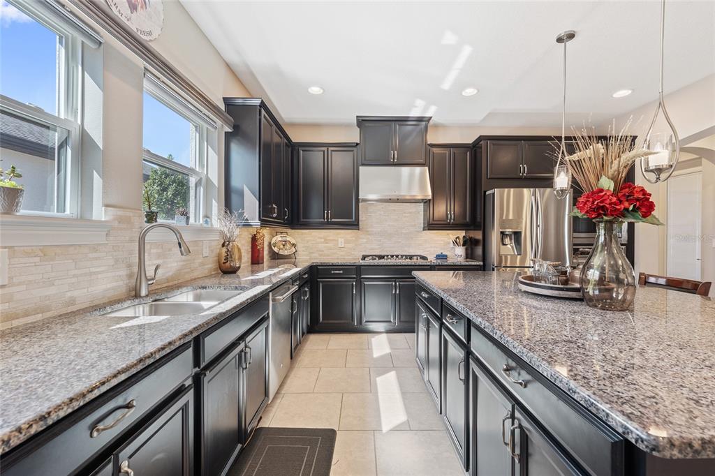 A kitchen features dark cabinets, granite countertops, stainless steel appliances, and a large center island — 2639 STARGRASS CIRCLE, CLERMONT, FL