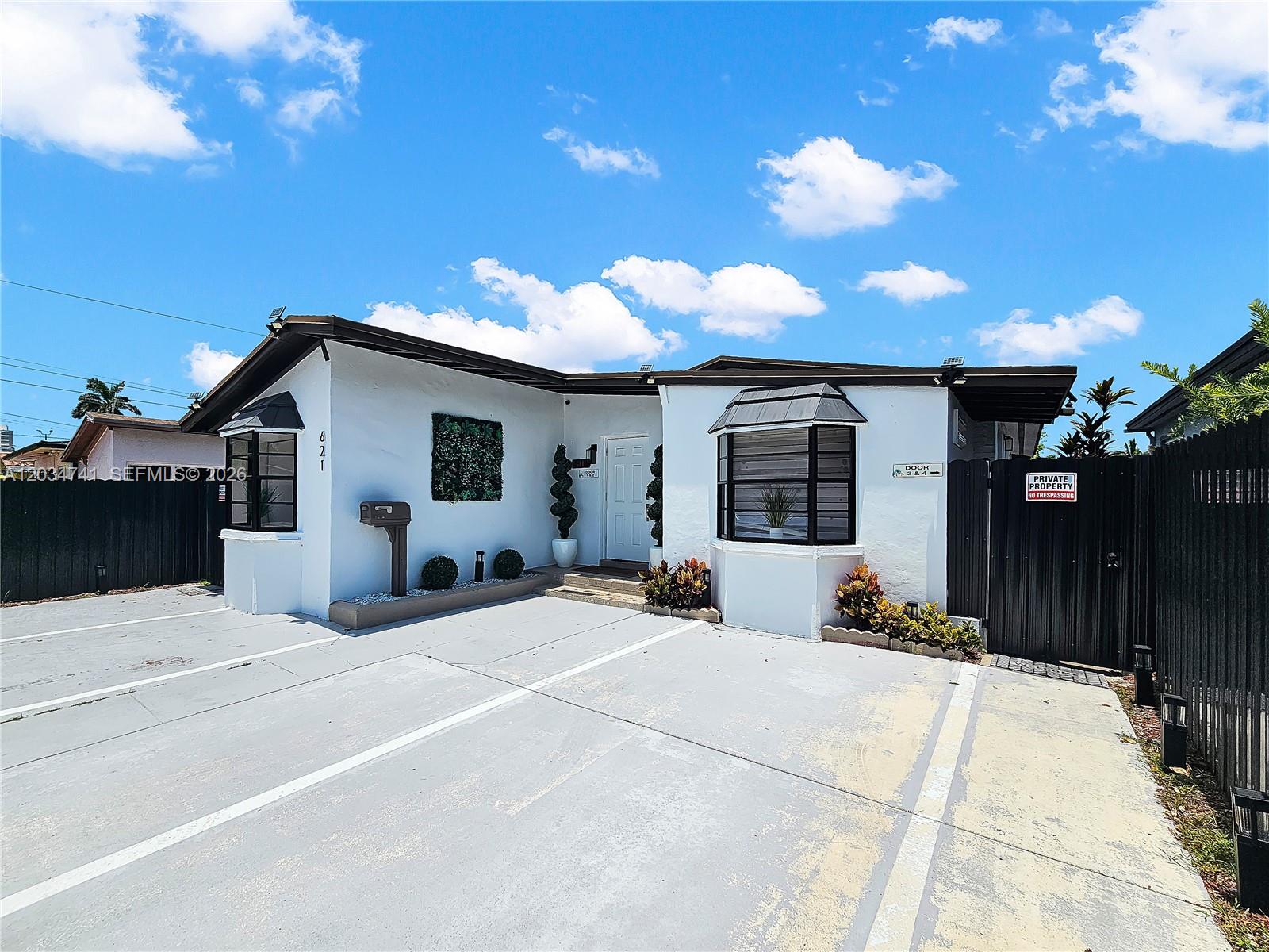 A white single-story building features a concrete parking area and a black wooden fence — 621 NW 59th Ave, Miami FL 33126, MIAMI, FL