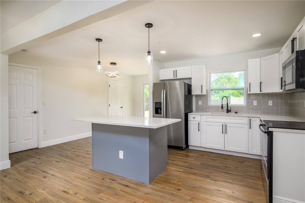 A kitchen features white cabinets, a gray island, stainless steel appliances, and wood-look flooring — 6711 S GABRIELLE STREET, TAMPA, FL