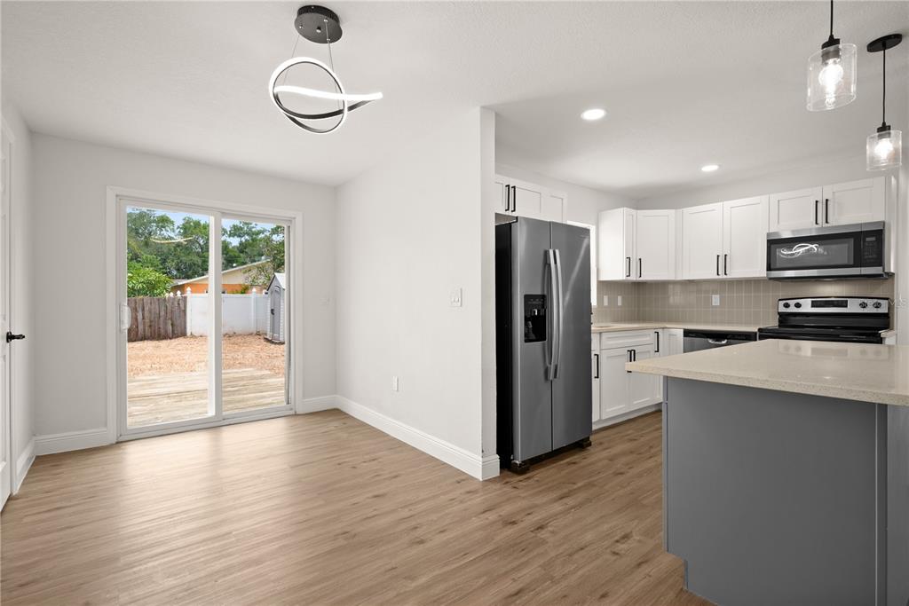 A kitchen with white cabinets, stainless steel appliances, and a gray island next to a dining area — 6711 S GABRIELLE STREET, TAMPA, FL