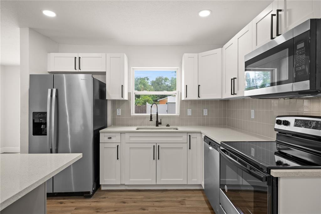 A kitchen features white cabinets, stainless steel appliances, a tile backsplash, and wood-look flooring — 6711 S GABRIELLE STREET, TAMPA, FL