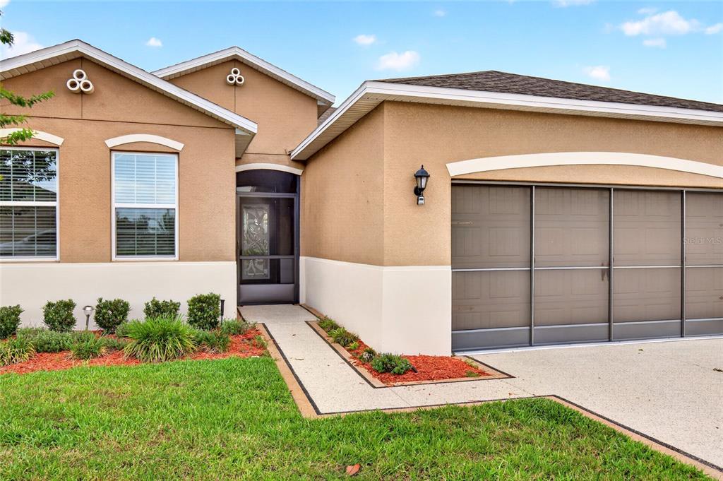 A tan stucco house features a front entrance with a screen door and a garage — 9149 SW 62ND TERRACE ROAD, OCALA, FL