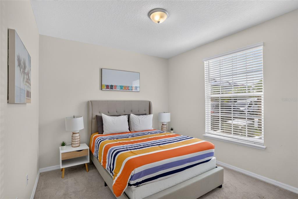 A bedroom features a bed with a striped comforter, two nightstands, and a large window — 7573 OAK SPRING LANE, DAVENPORT, FL