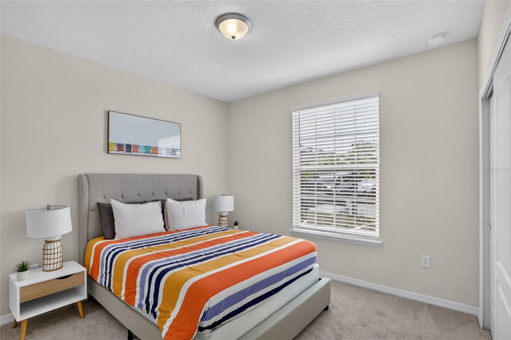 A bedroom features a bed with a striped comforter, a nightstand, and a window — 7573 OAK SPRING LANE, DAVENPORT, FL