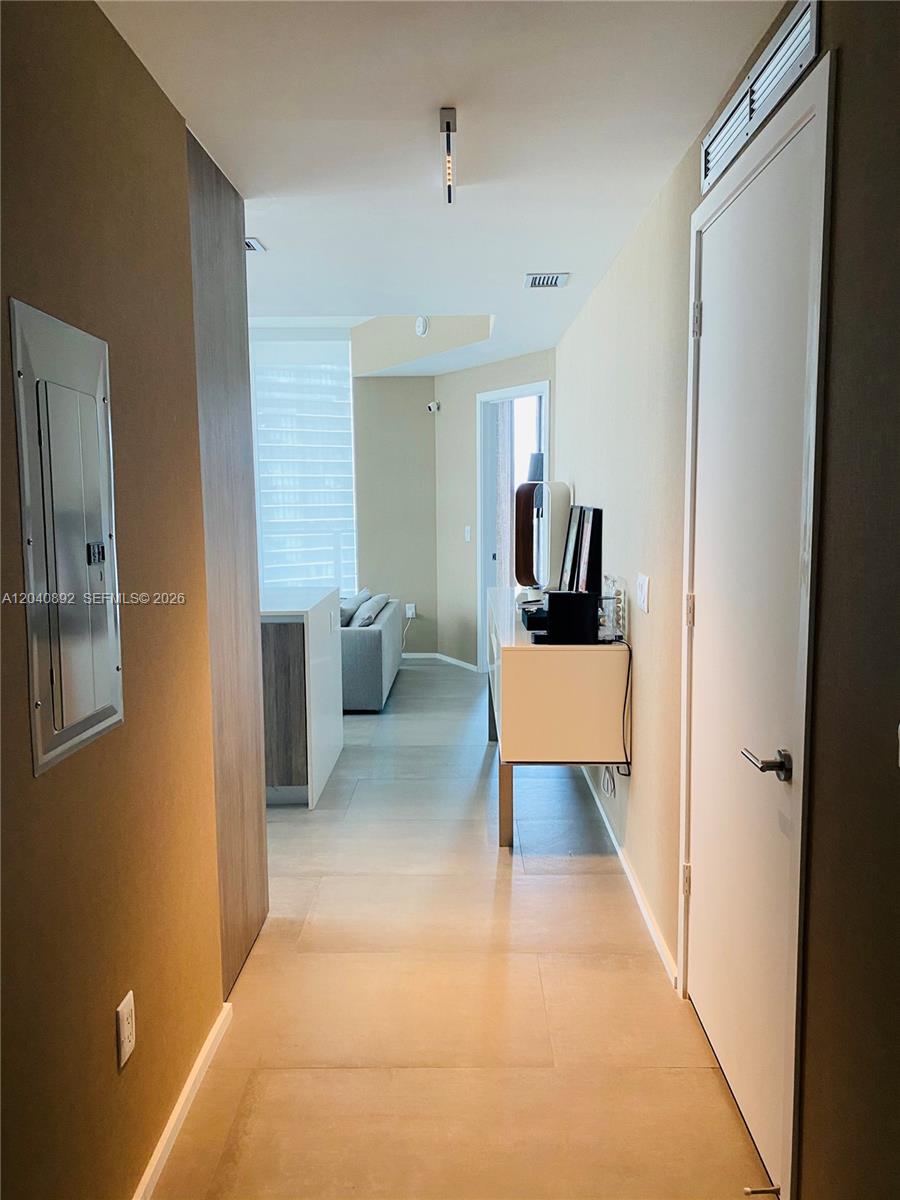 A hallway with light tile flooring leads toward a living area with a white console — MIAMI, FL