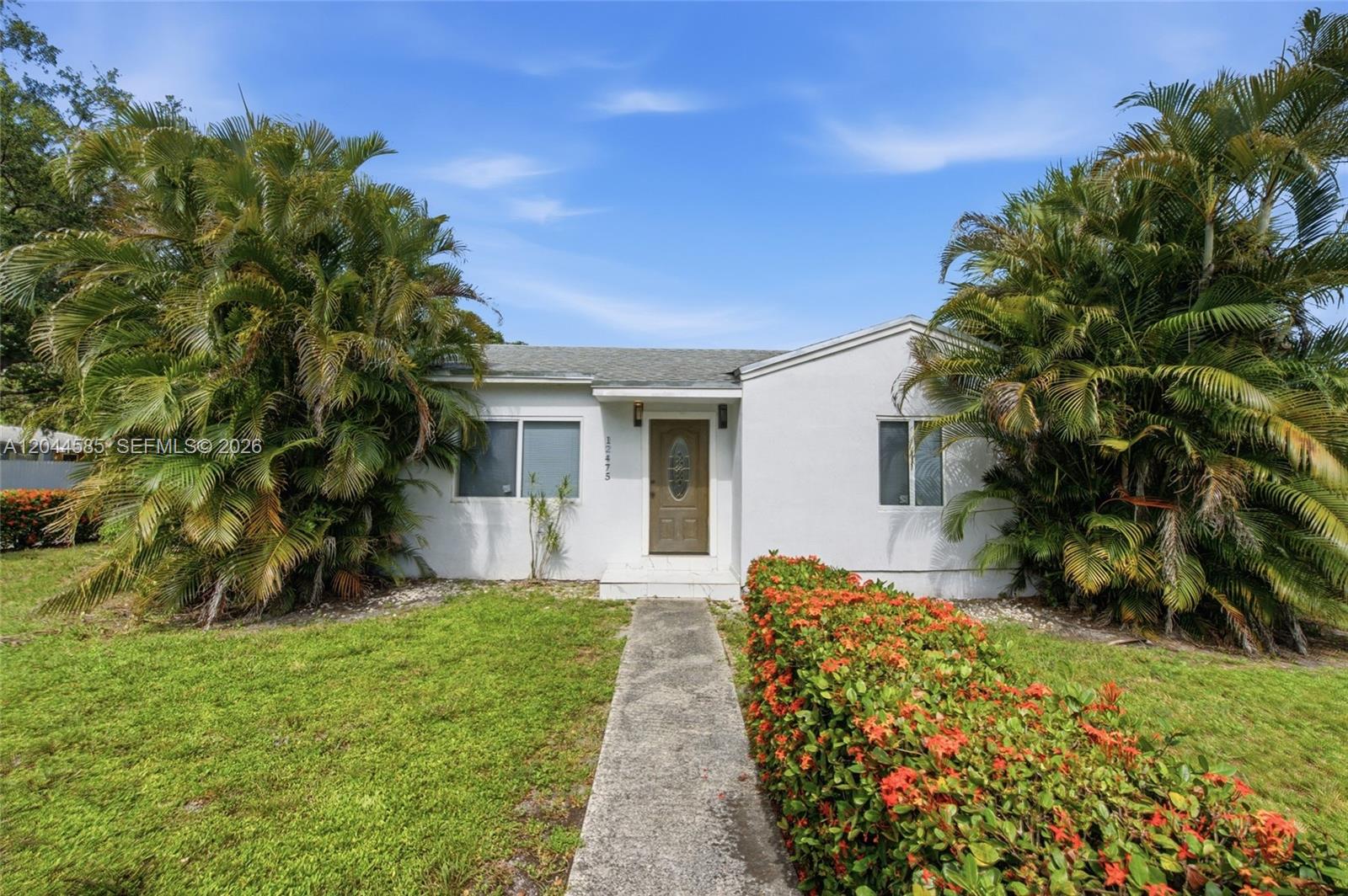 A white, single-story house features a concrete walkway, palm trees, and a flowering hedge — 12475 NW 10th Ave, North Miami FL 33168, NORTH MIAMI, FL