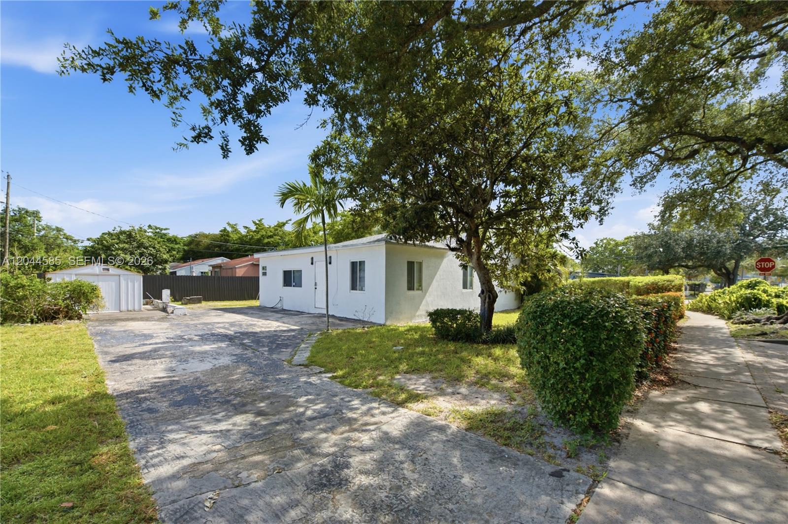A white single-story house features a concrete driveway, a small shed, and mature trees — 12475 NW 10th Ave, North Miami FL 33168, NORTH MIAMI, FL