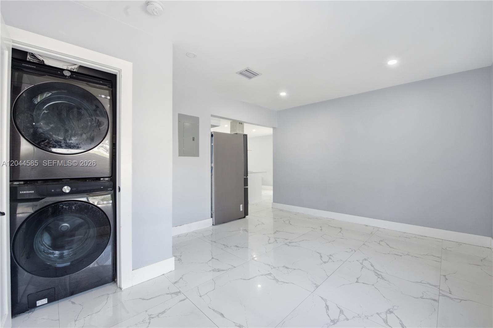 A room with white marble-patterned tile floors, a stacked washer-dryer, and a refrigerator — 12475 NW 10th Ave, North Miami FL 33168, NORTH MIAMI, FL