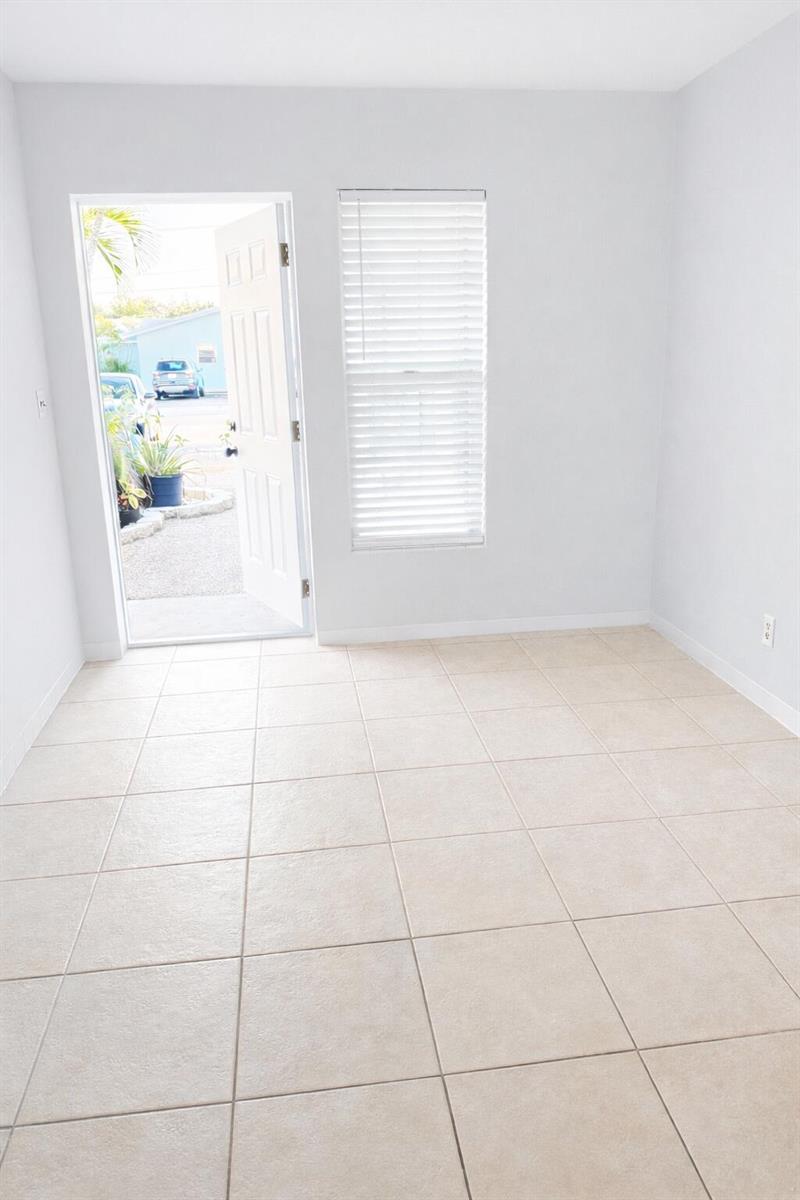 An empty room with light-colored tile flooring, white walls, a window, and an open door — 1017 SE 3rd Street # 3, Deerfield Beach FL 33441, DEERFIELD BEACH, FL