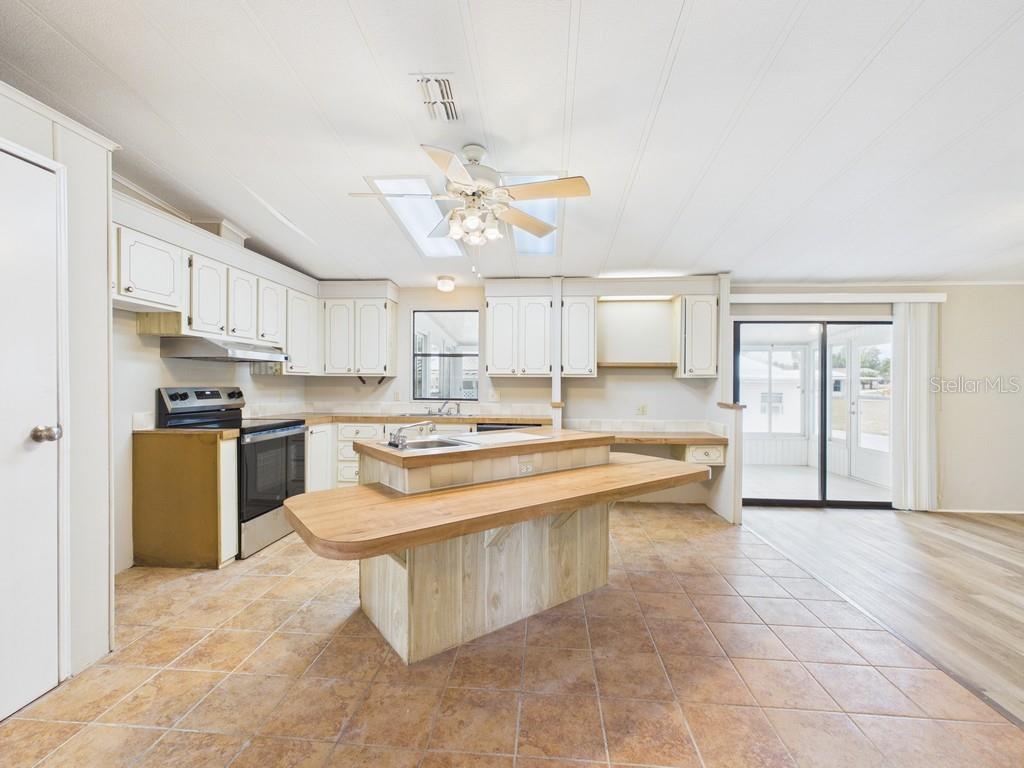 A kitchen with white cabinets, a wood-topped island, and tile flooring next to a sunroom — 9212 DENMARSH DRIVE, BROOKSVILLE, FL