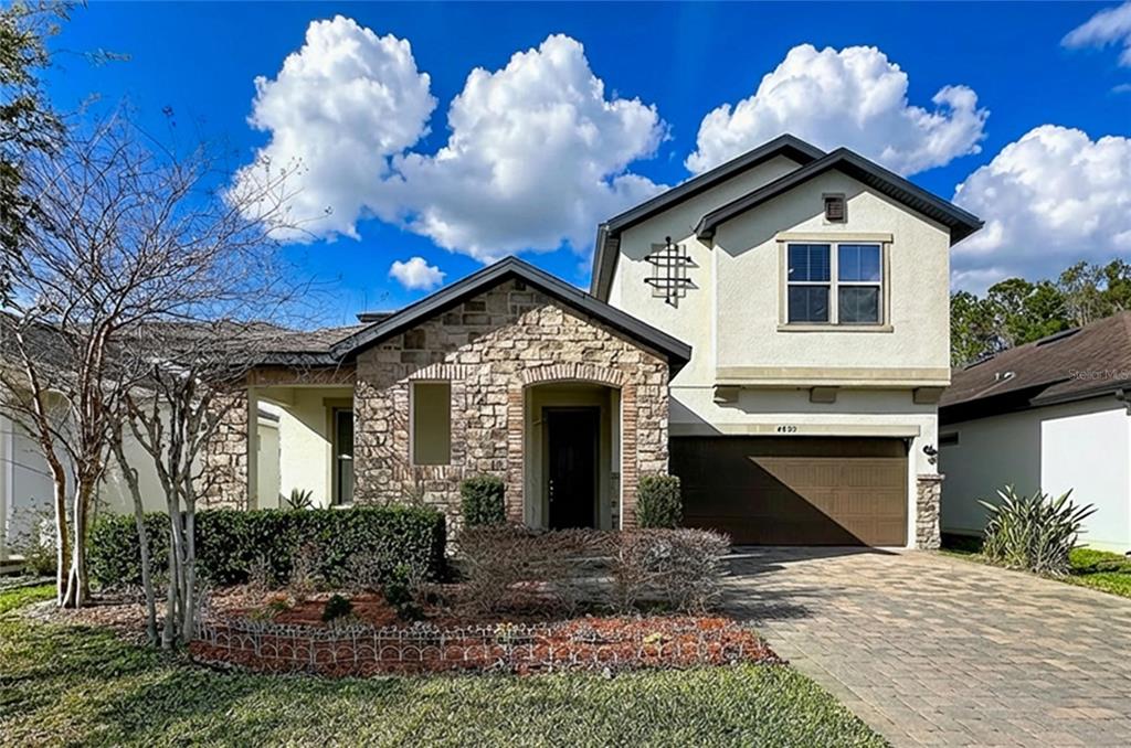 A two-story house features a stone facade, a brown garage door, and a paved driveway — 4892 ECHO COURT UNIT 44, OVIEDO, FL