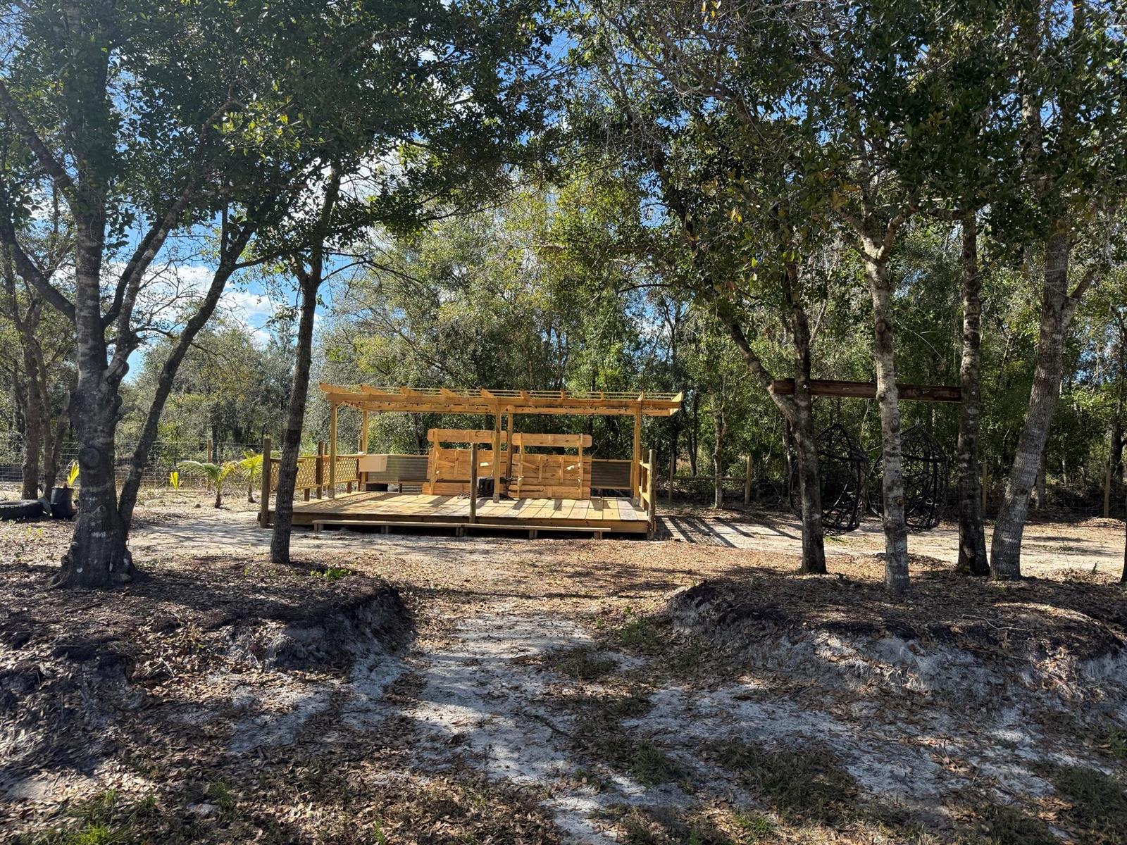 A wooden deck with a pergola and seating sits in a wooded, sandy backyard — 17618 NW 286th Street, Okeechobee FL 34972, OKEECHOBEE, FL