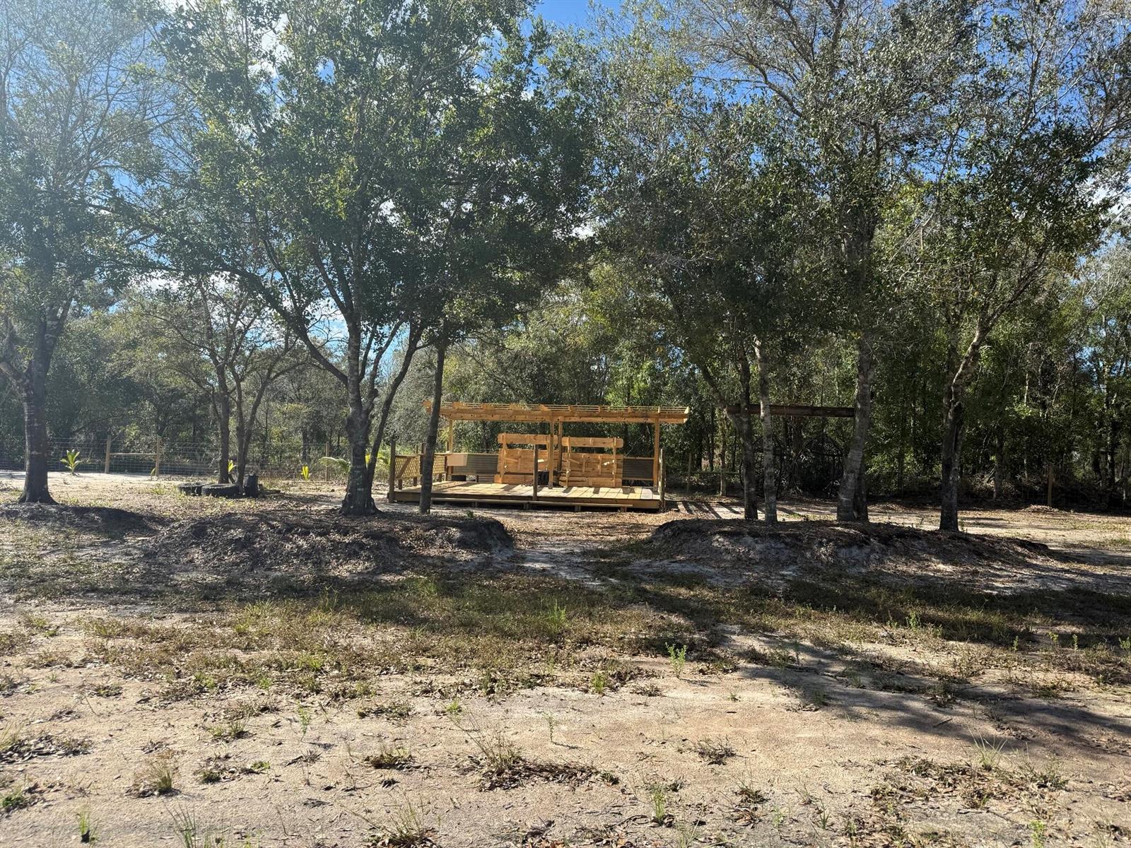 A wooden deck with a pergola and built-in seating sits among trees in a yard — 17618 NW 286th Street, Okeechobee FL 34972, OKEECHOBEE, FL