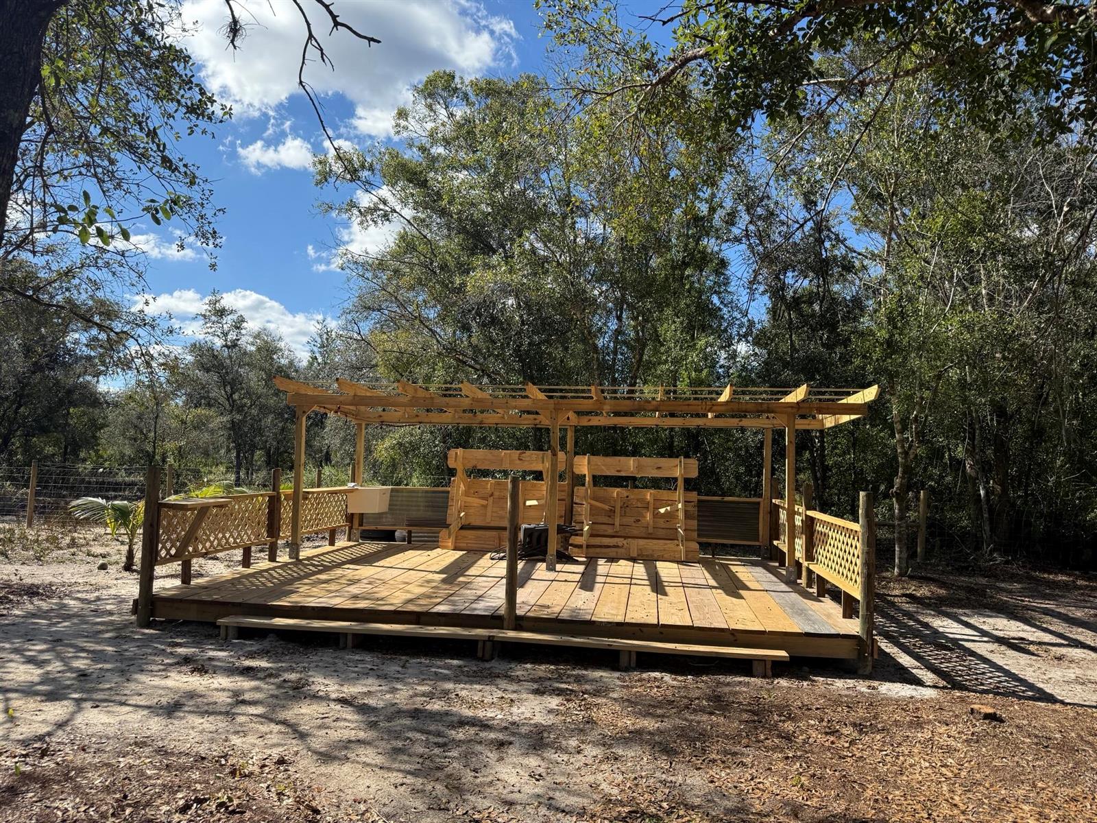 A wooden deck with a pergola and built-in seating sits in a wooded outdoor area — 17618 NW 286th Street, Okeechobee FL 34972, OKEECHOBEE, FL