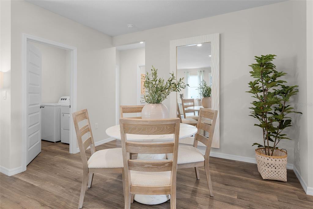 A dining area features a round table, four wooden chairs, a large mirror, and a plant — 8464 FOX DEN COVE, LAKELAND, FL
