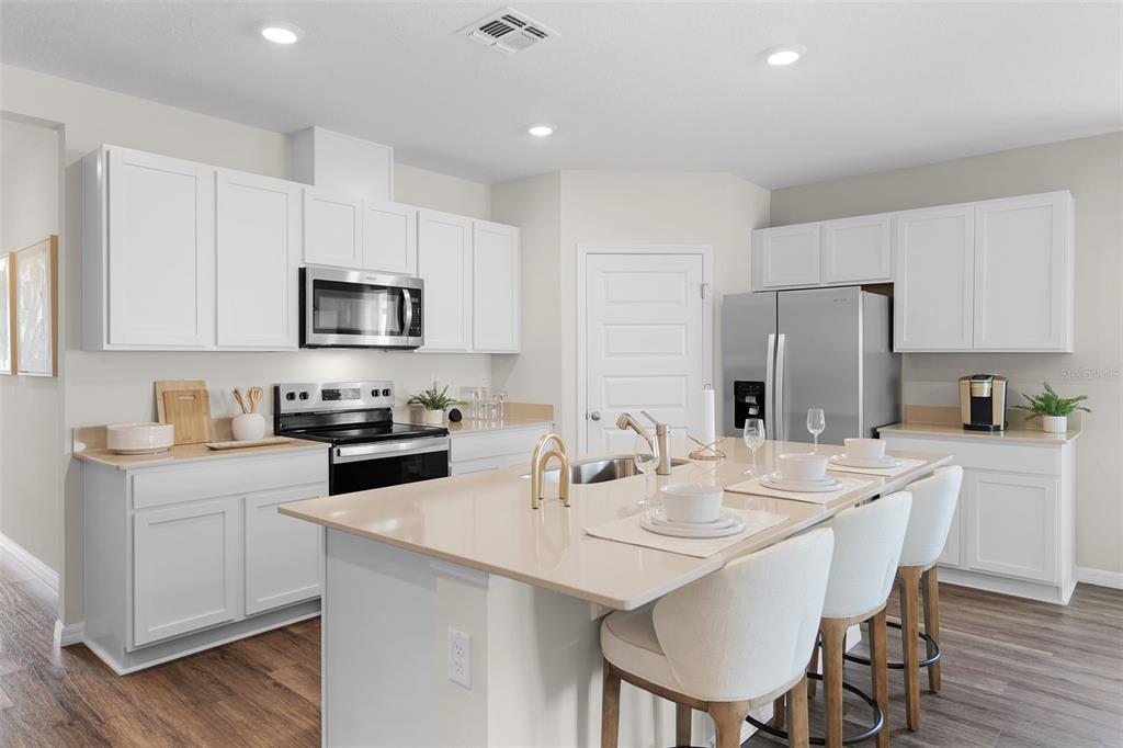 A modern kitchen features white cabinets, stainless steel appliances, and a large central island — 8464 FOX DEN COVE, LAKELAND, FL