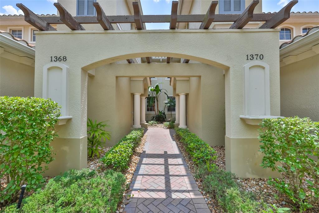 A brick walkway leads through a covered pergola entrance between two residential building units — 1368 EMERALD DUNES DRIVE, SUN CITY CENTER, FL
