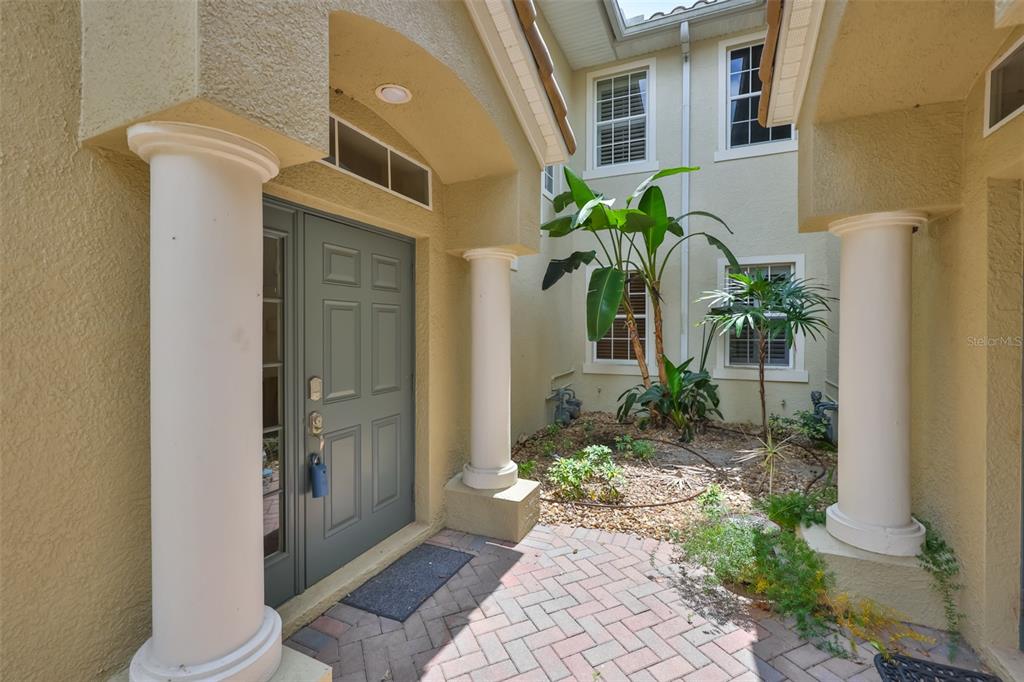 An exterior view of a home entrance with a brick patio, columns, and a courtyard — 1368 EMERALD DUNES DRIVE, SUN CITY CENTER, FL