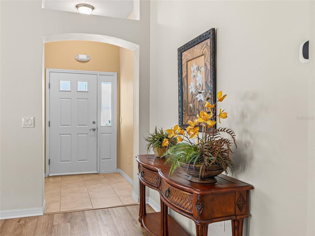 An entryway features a wooden console table, floral decor, and a white front door — 1134 SOUTHERN SUN DRIVE, THE VILLAGES, FL