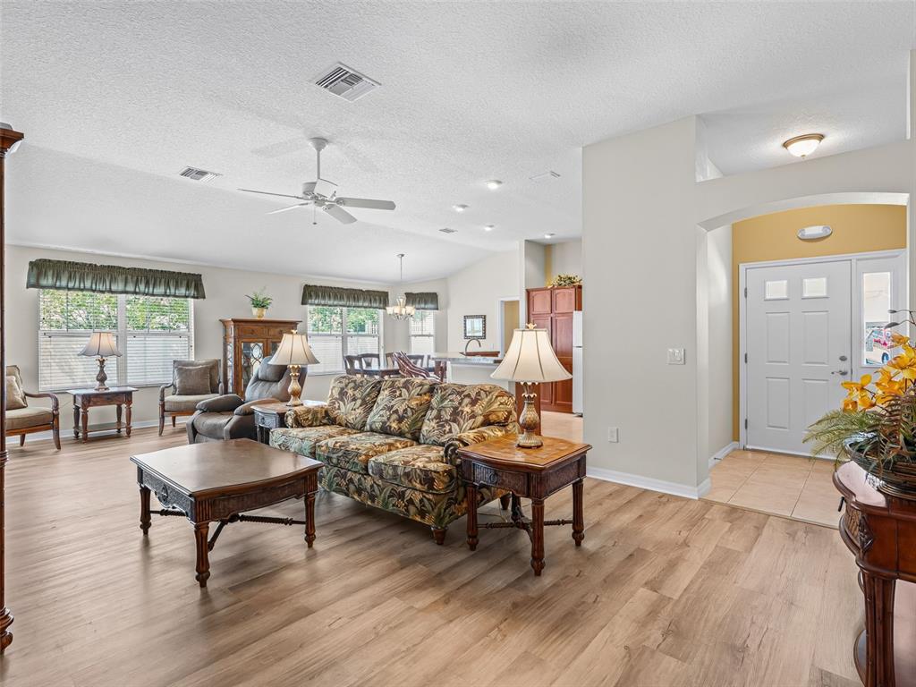 A living room with wood-look flooring, a floral sofa, and an adjacent entryway — 1134 SOUTHERN SUN DRIVE, THE VILLAGES, FL