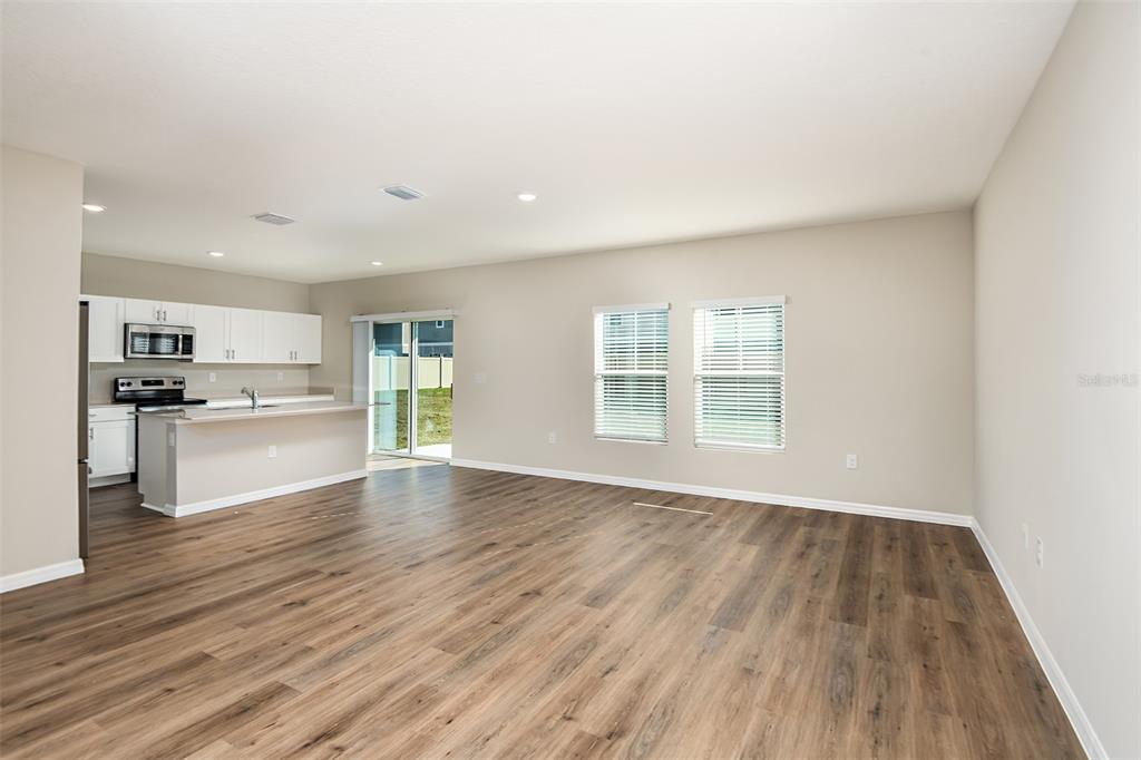 An open-concept kitchen and living area with wood-look flooring and white cabinetry — 5437 SAN PIETRO DRIVE, WINTER HAVEN, FL