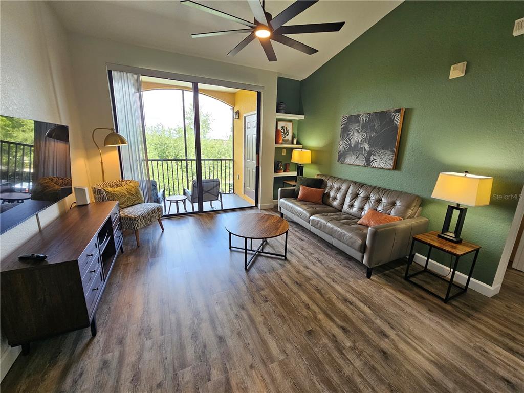 A living room features a green accent wall, leather sofa, wood flooring, and balcony access — 8335 38TH STREET CIRCLE E UNIT 305, SARASOTA, FL