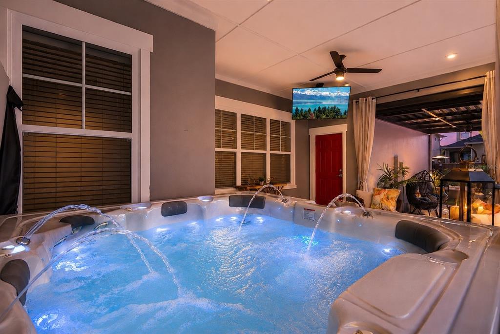 A hot tub with illuminated water jets sits on a covered patio with a television — 13308 STODDART AVENUE, ORLANDO, FL