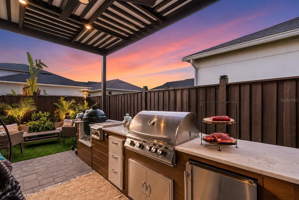 An outdoor kitchen with a stainless steel grill and stone countertop sits under a pergola — 13308 STODDART AVENUE, ORLANDO, FL