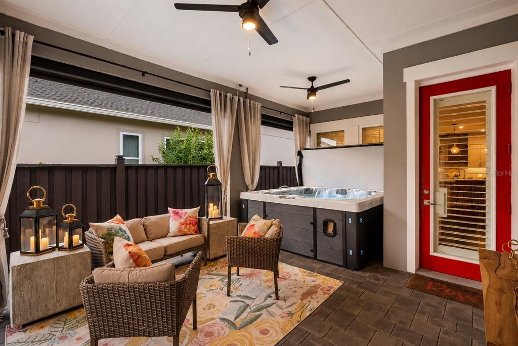 A covered patio features a hot tub, wicker furniture, a floral rug, and a red door — 13308 STODDART AVENUE, ORLANDO, FL