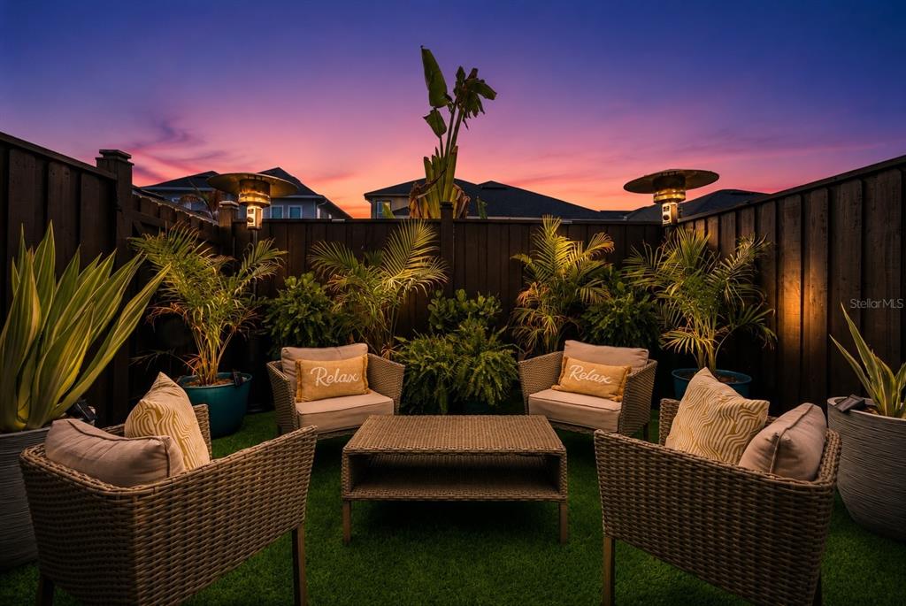 An outdoor patio area features wicker furniture, potted plants, and a fence at sunset — 13308 STODDART AVENUE, ORLANDO, FL