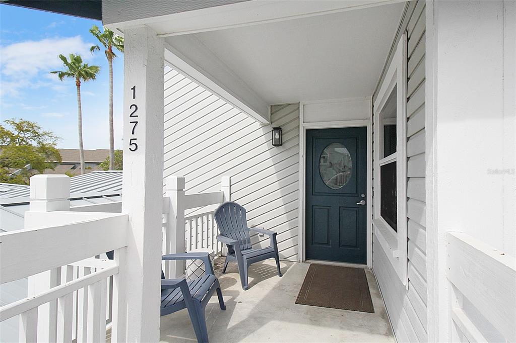 A covered porch features two blue chairs, a dark door, and white siding — 1275 SIESTA BAYSIDE DRIVE UNIT 1275-B, SARASOTA, FL