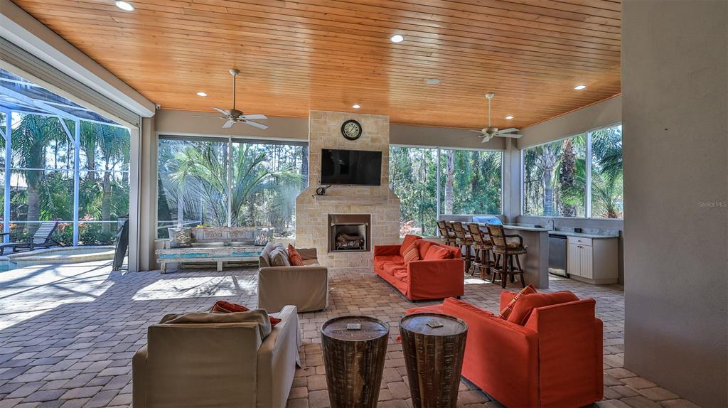 A covered outdoor patio features a stone fireplace, orange seating, and a built-in bar area — 2904 Palma LANE, NEW SMYRNA BEACH, FL