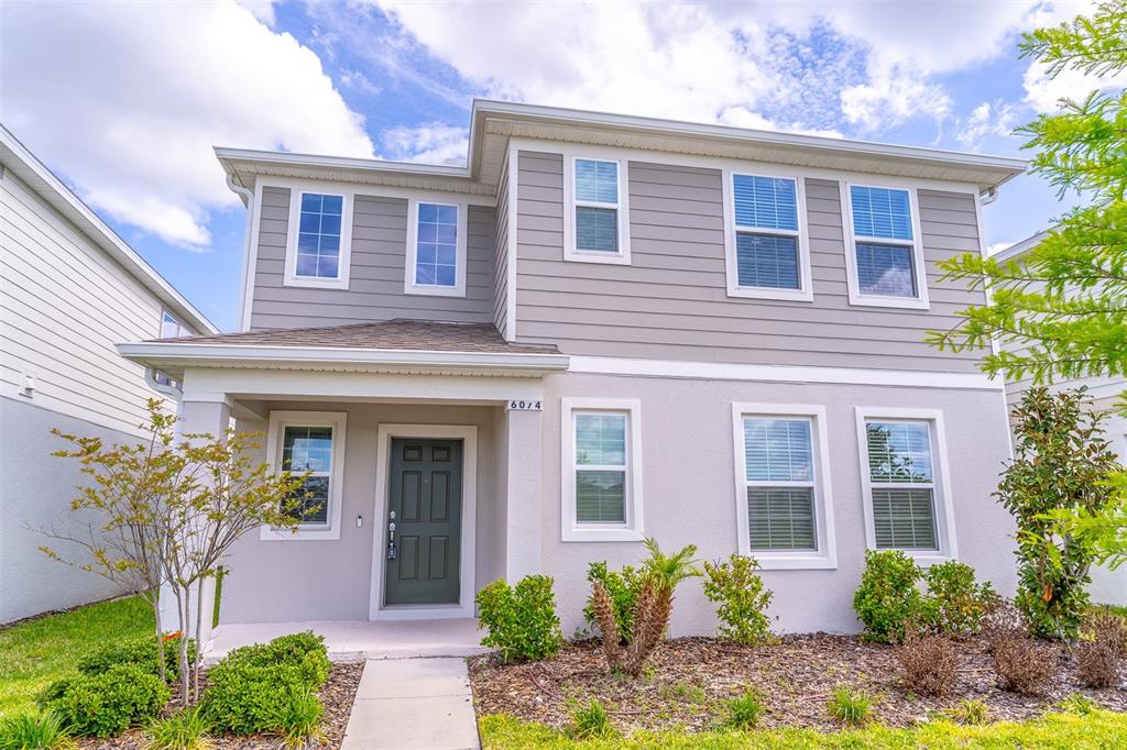 A two-story house with gray horizontal siding, a covered porch, and a dark front door — 6074 WINDY LEAF ALLEY, ST CLOUD, FL
